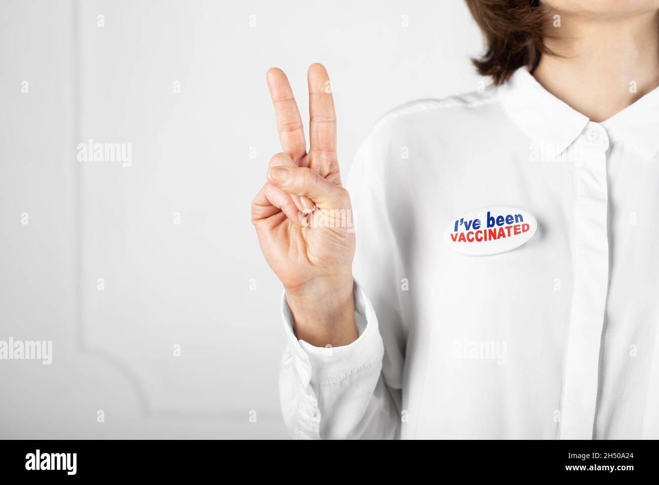 Media età femmina caucasica in camicia bianca con bottone spilla sono stato vaccinato mostrando V gesto Foto Stock