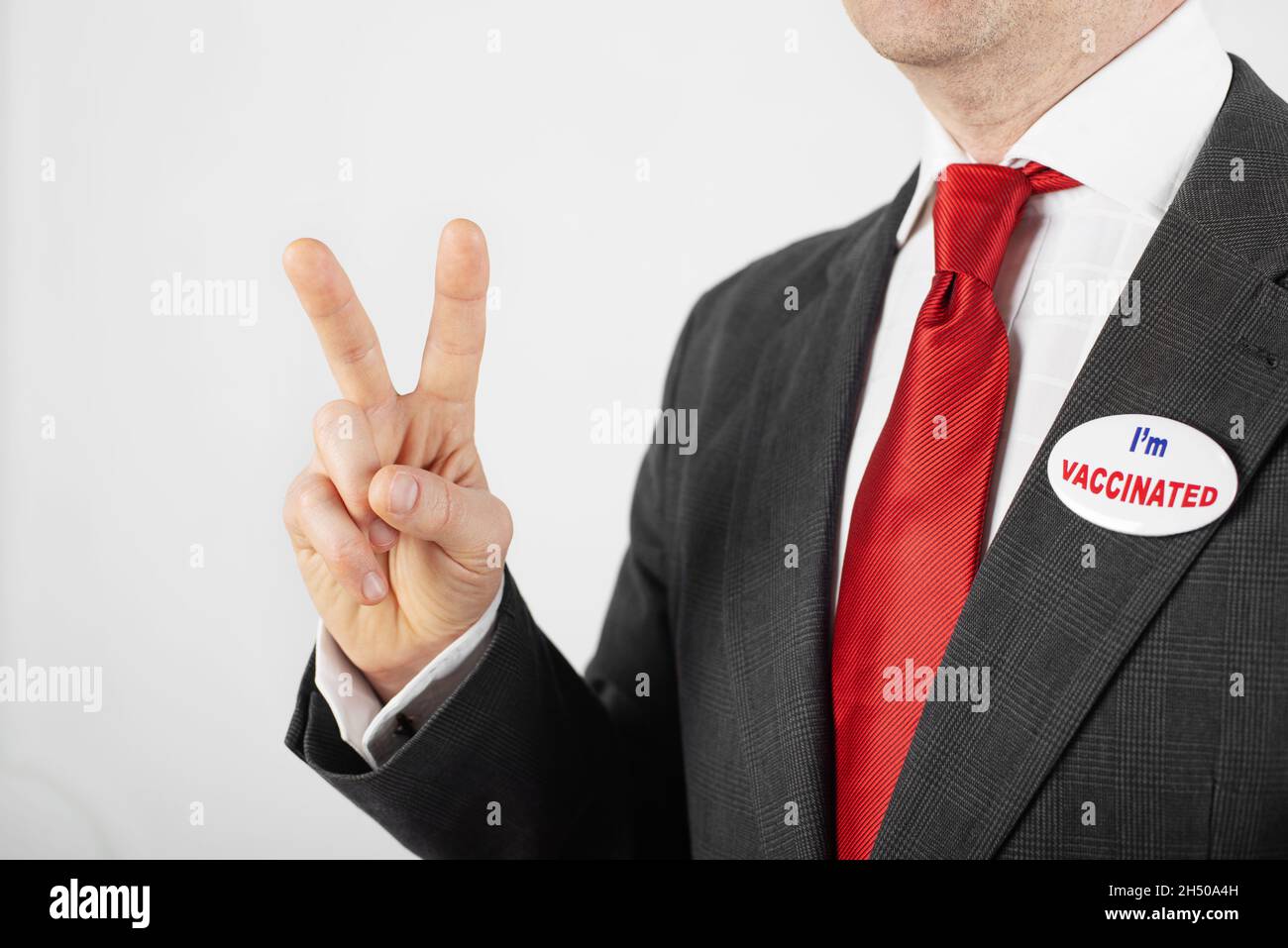 Medio età uomo caucasico in tuta con bottone pin sono vaccinato mostrando V gesto Foto Stock
