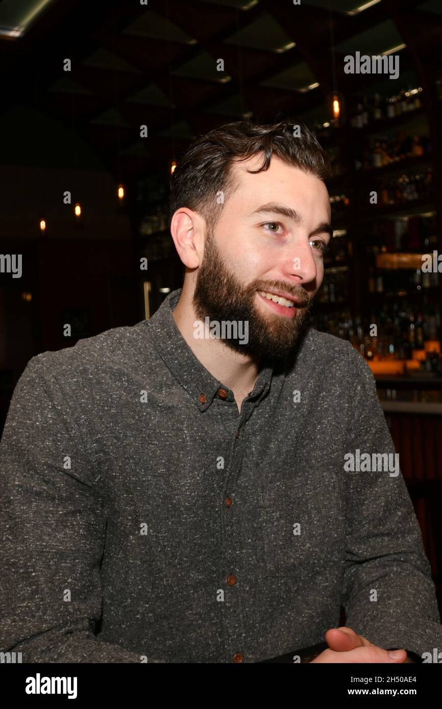 L'uomo in bearded bianco siede in un ristorante di notte con le espressioni facciali differenti. Foto Stock