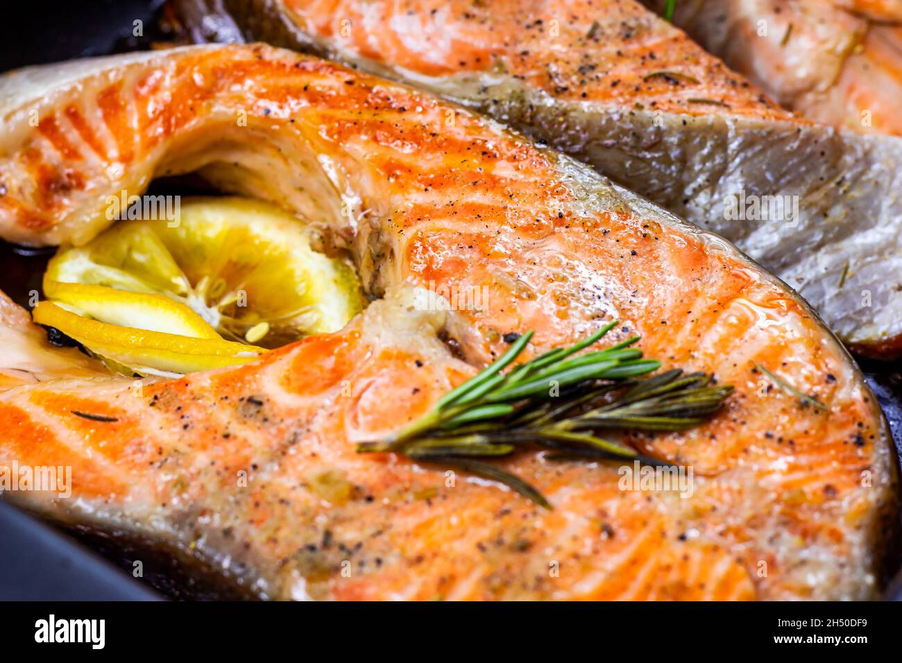 Bistecche di pesce di salmone rosso arrostito fresco con erbe, spezie e limone su fondo piatto di metallo nero in cucina. Foto Stock