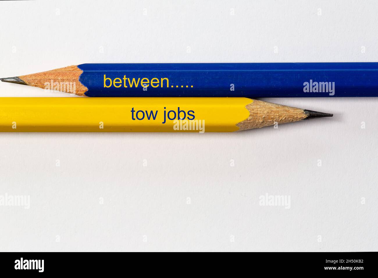 due matite affilate in blu e giallo puntano in direzioni diverse isolate su sfondo bianco con la frase: tra lavori di traino Foto Stock