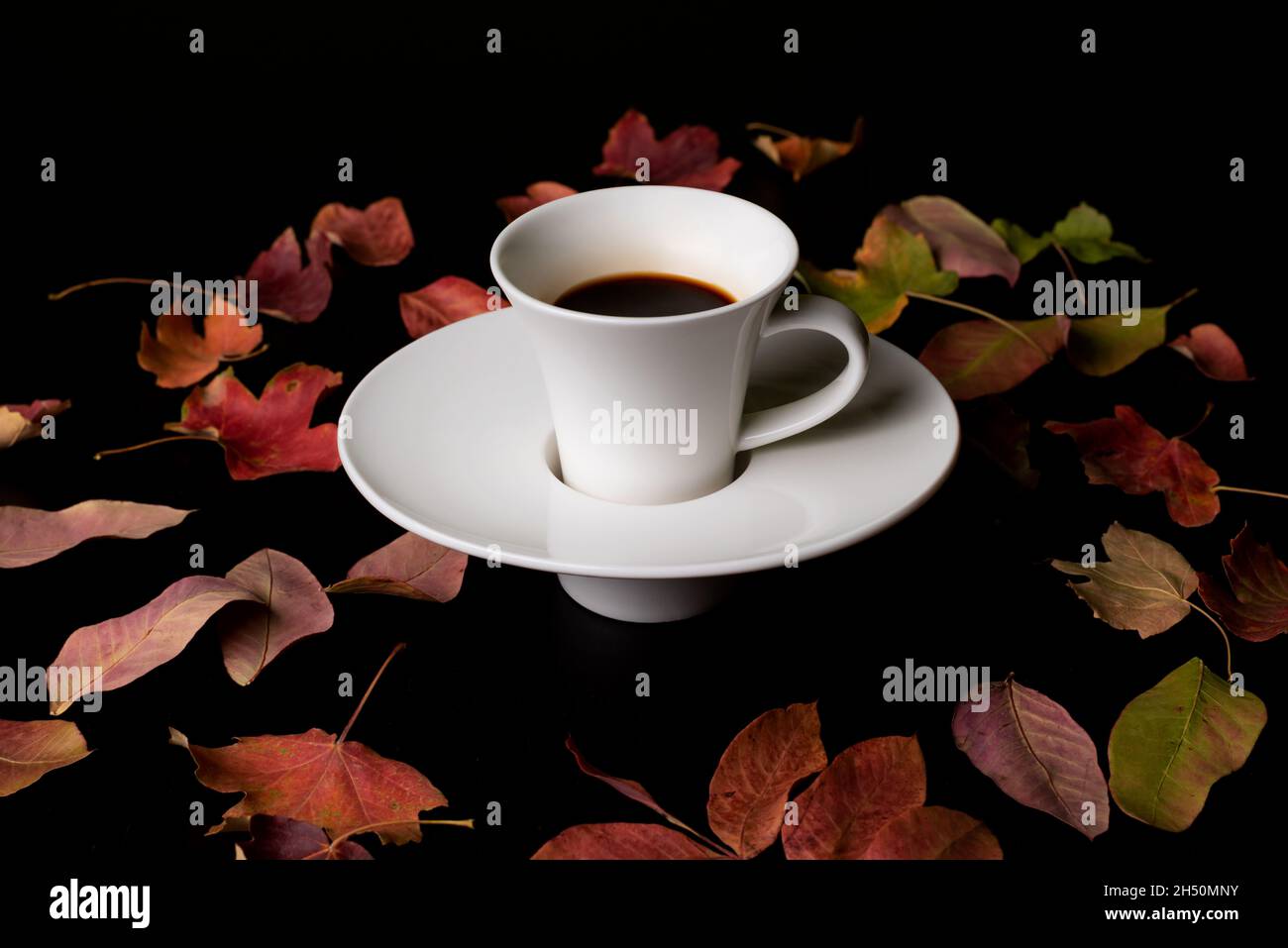 Tazza di caffè con alcune ciambelle glassate, accanto ad alcune foglie secche autunnali intorno ad essa. Foto Stock