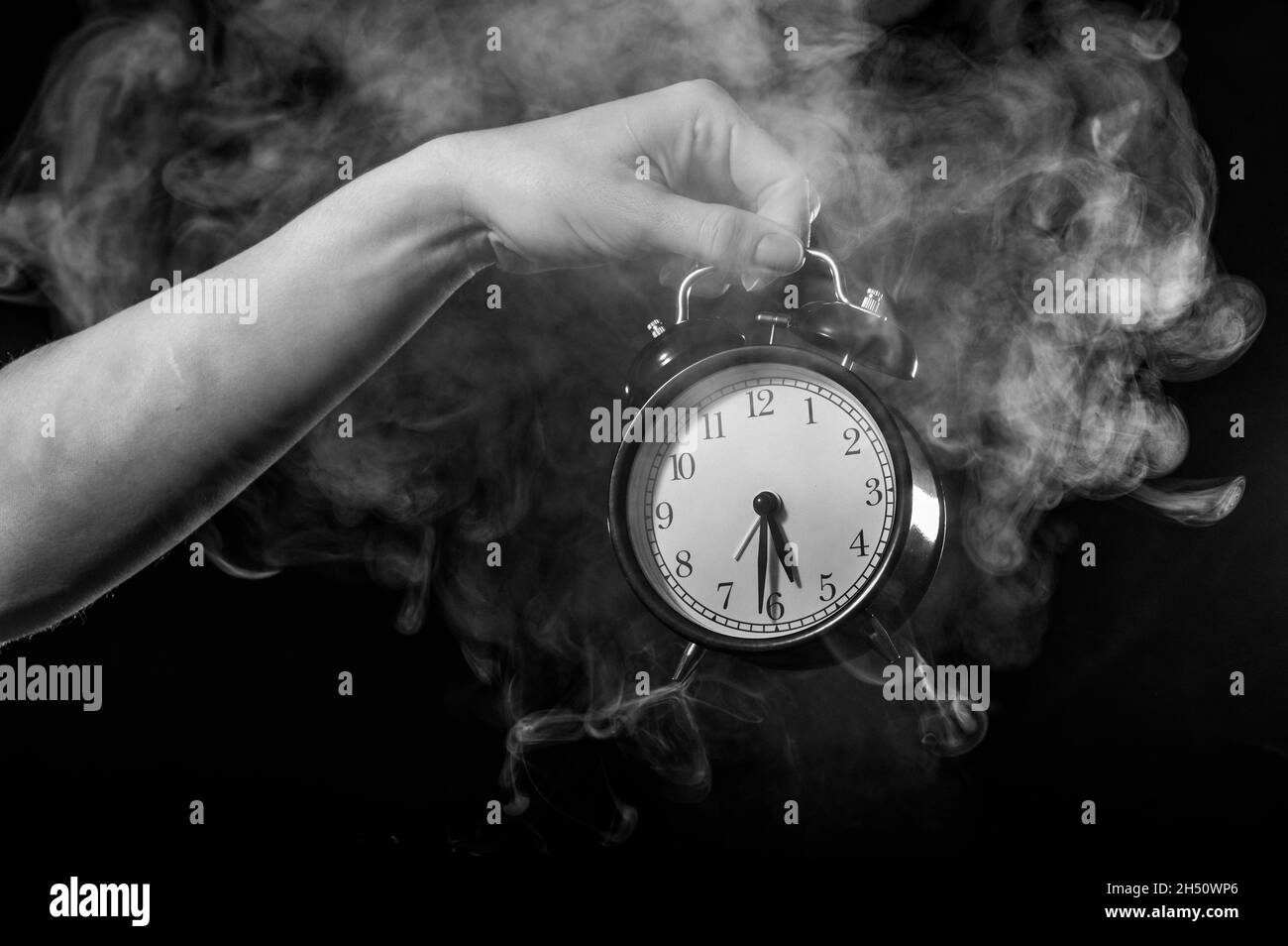 Una donna tiene una sveglia in uno studio pieno di fumo. La nebbia bianca avvolse un orologio meccanico retrò rotondo. Foto Stock