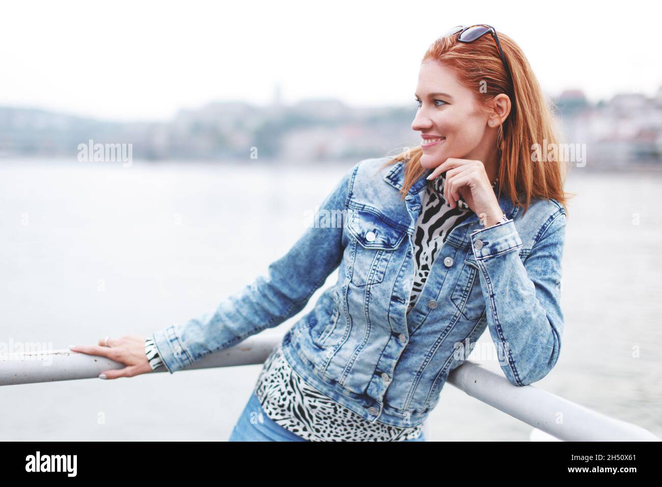 Felice giovane rossa caucasica urbana donna posando in riva al fiume, guardando via Foto Stock