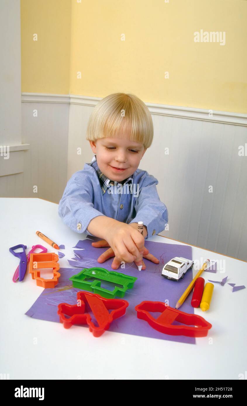 Un bambino di tre anni traccia intorno alla sua mano con pastelli al tavolo della cucina con forniture d'arte. Foto Stock