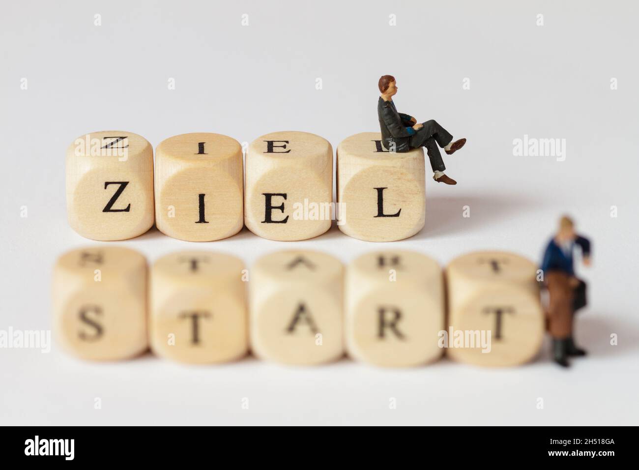 Piccole figure in plastica con parole fatte da cubi di lettere. La parola tedesca per obiettivo e per inizio può essere letta Foto Stock