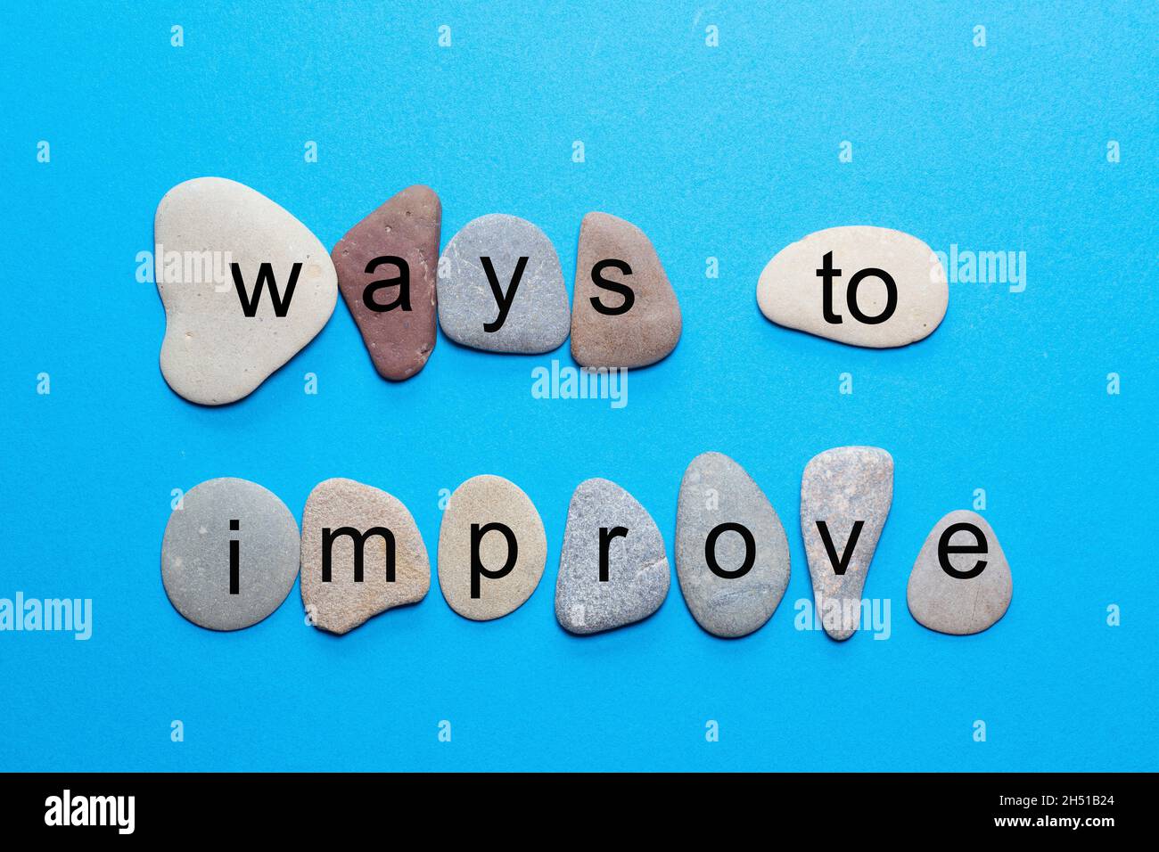 La frase modi per migliorare si leva come lettere singole su pietre naturali lisce con colori più naturali su uno sfondo blu Foto Stock