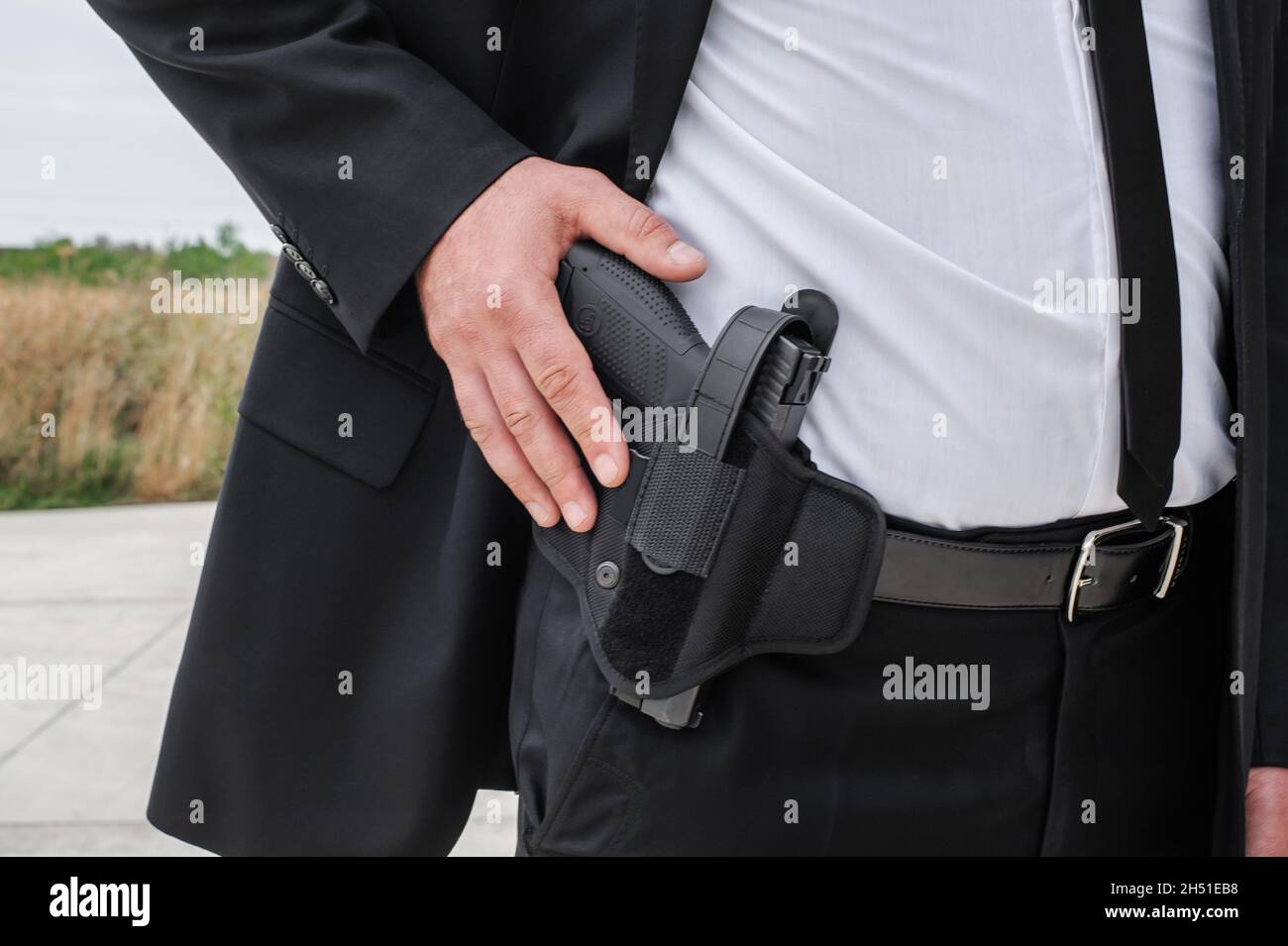 Vista dettagliata dell'agente spia maschio Bodyguard mano con pistola nel nastro bandolier. Polizia di sicurezza in abito nero civile Foto Stock