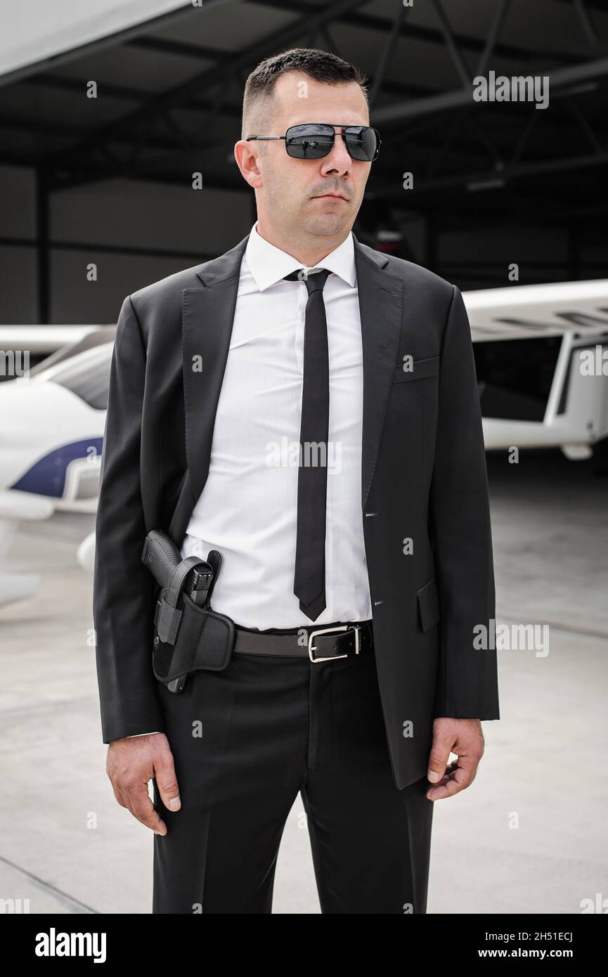 Bodyguard professionale agente spia maschile con pistola. Polizia di sicurezza in abito nero civile con occhiali da sole. Chiudere la protezione di sicurezza Foto Stock