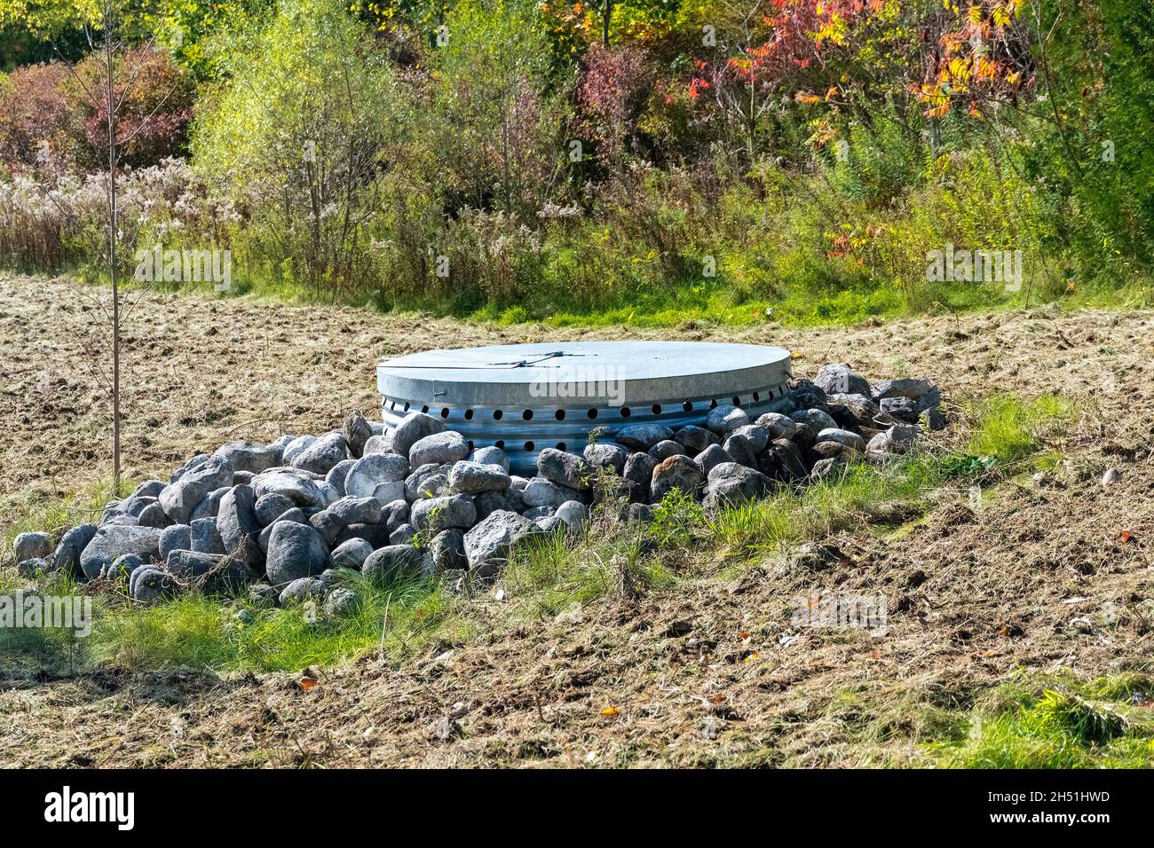 Botola di comunicazione sul campo, recintata da pietre provenienti da trattori che eseguono lavori su seminativi Foto Stock