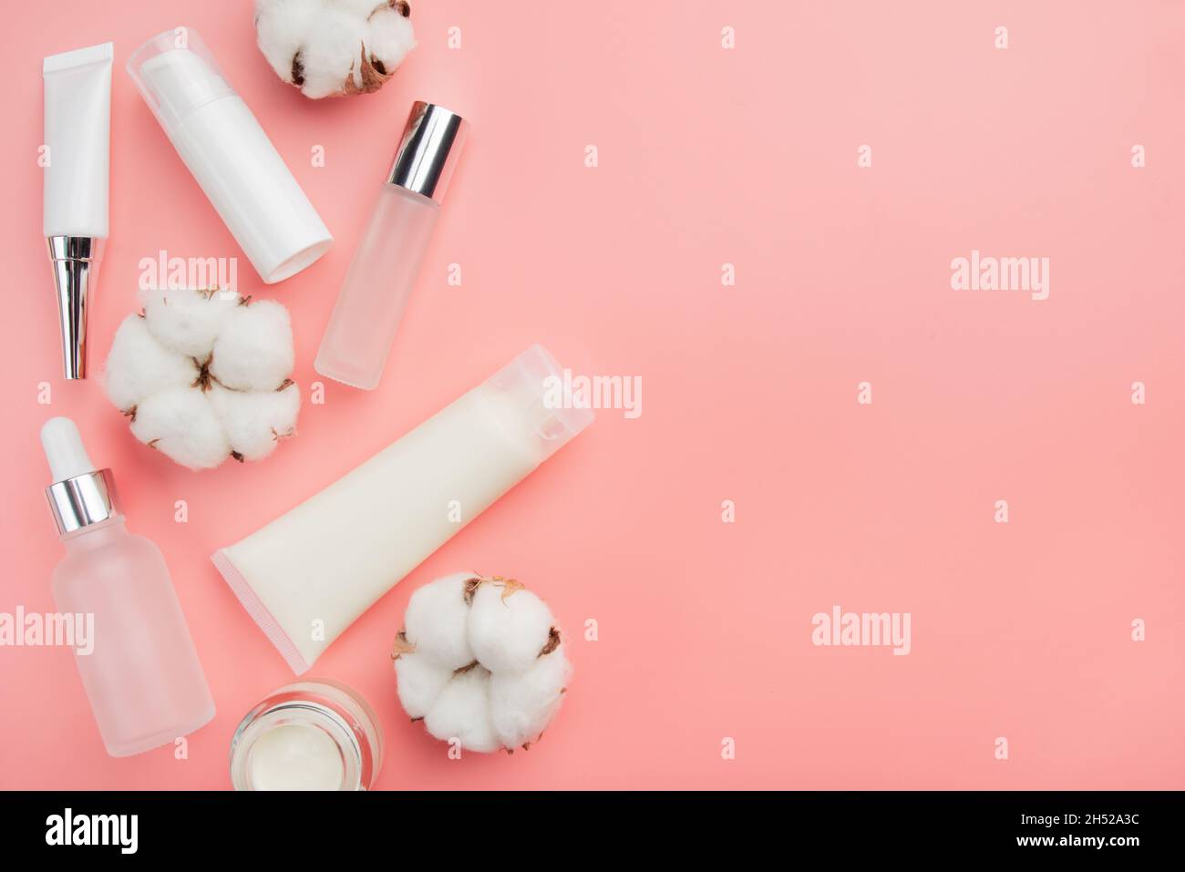 Bottiglie cosmetiche in vetro e plastica su sfondo rosa con biglie di cotone. Spazio di copia per il testo Foto Stock