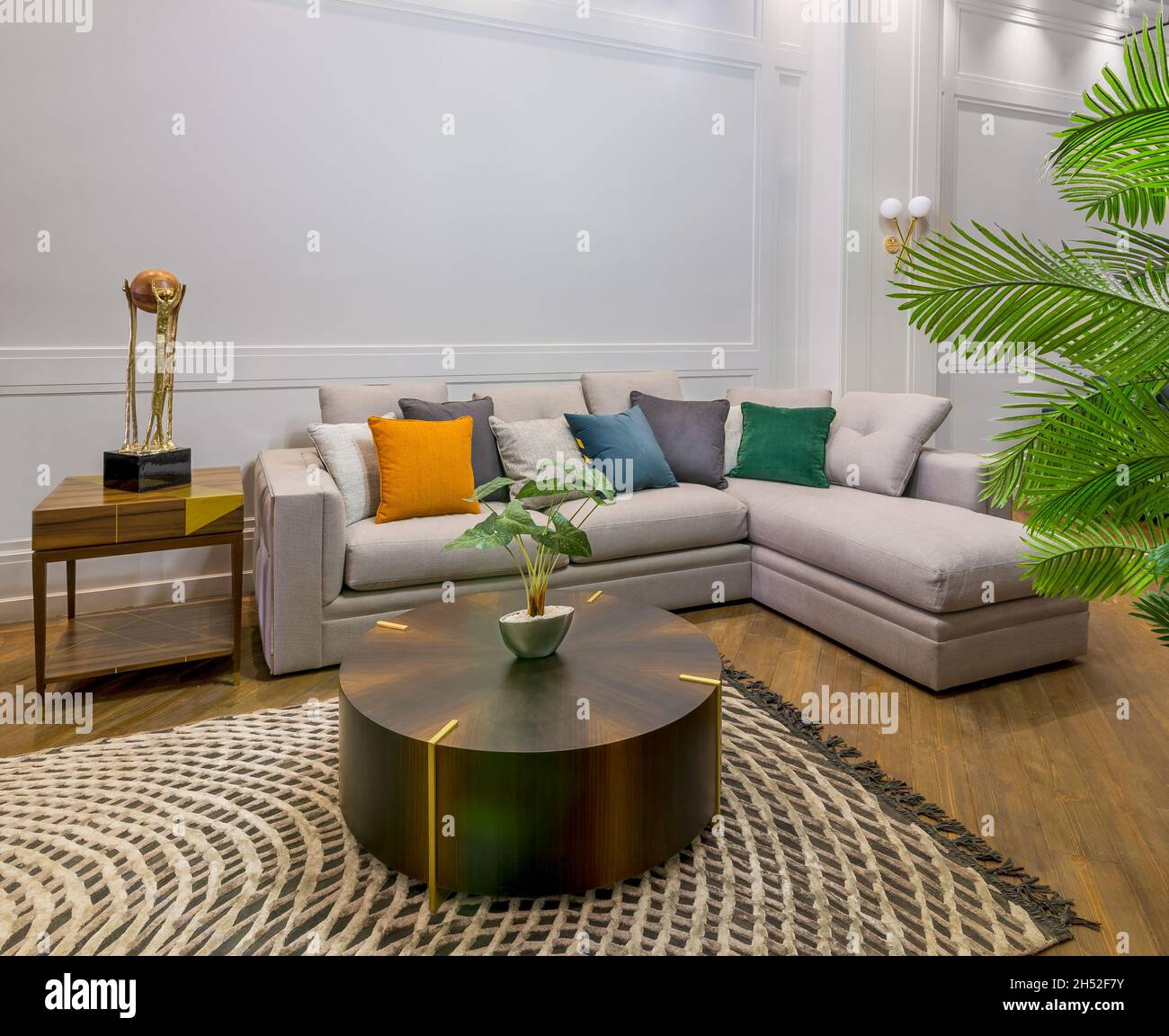 Comodo divano grigio con cuscini colorati posto vicino al tavolo su tappeto  in spaziosa camera moderna con poltrone e piante in vaso verde Foto stock -  Alamy