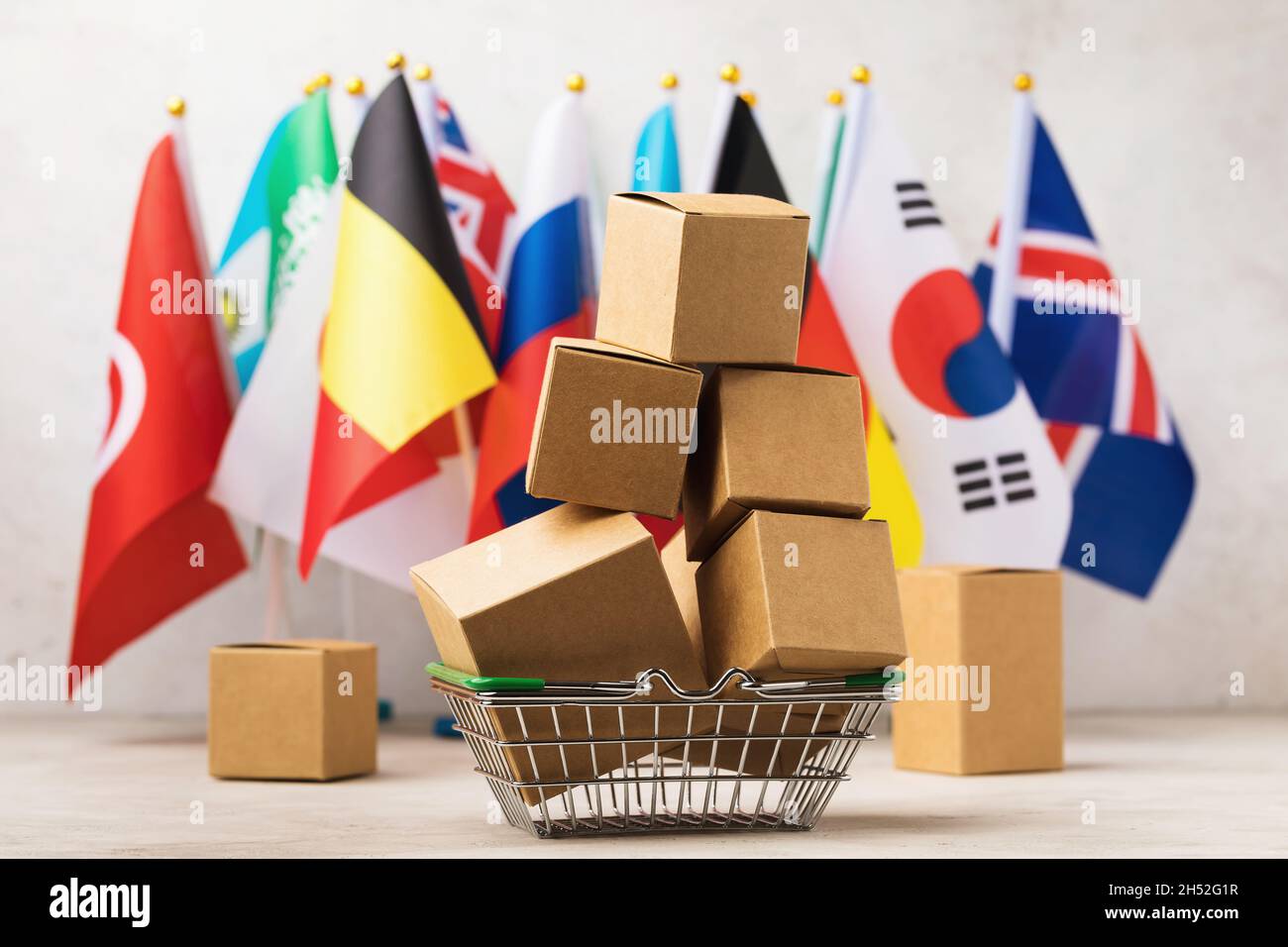 Scatole di carta in un cestino di alimentari sullo sfondo di bandiere di diversi paesi, il concetto di grande consumo di beni nel mondo Foto Stock