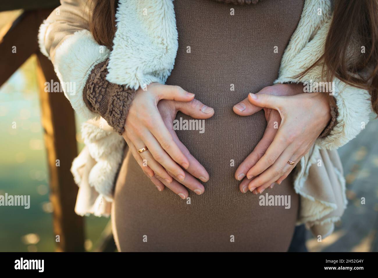 Mani di membri della famiglia che tengono una pancia di donna incinta. Infezione da coronavirus, vaccinazione e protezione durante la gravidanza Foto Stock
