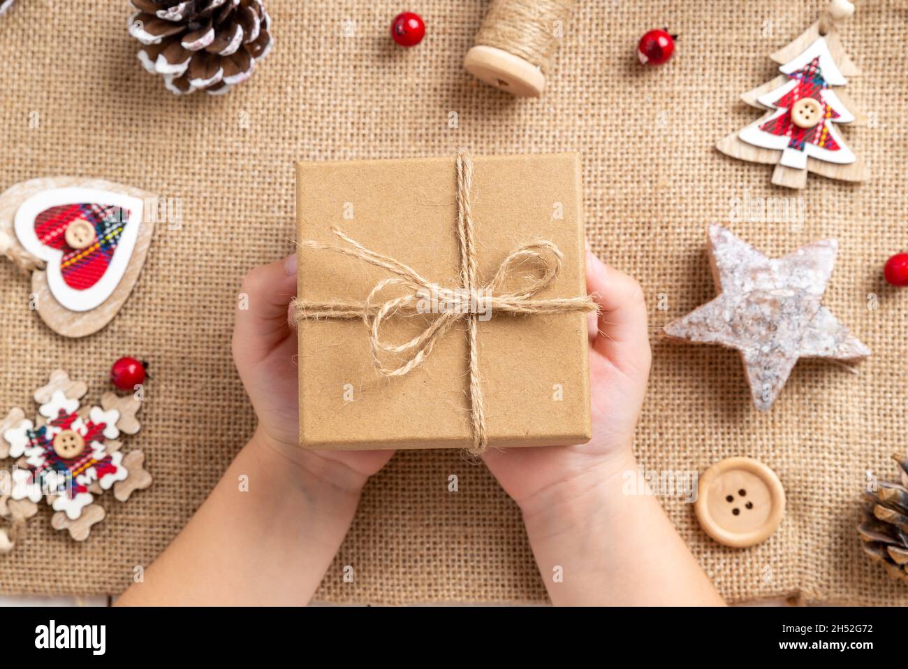 Le mani dei bambini tengono un regalo di Natale appena fatto. Tavolo con decorazioni natalizie. Vista dall'alto, composizione di giacitura piatta Foto Stock