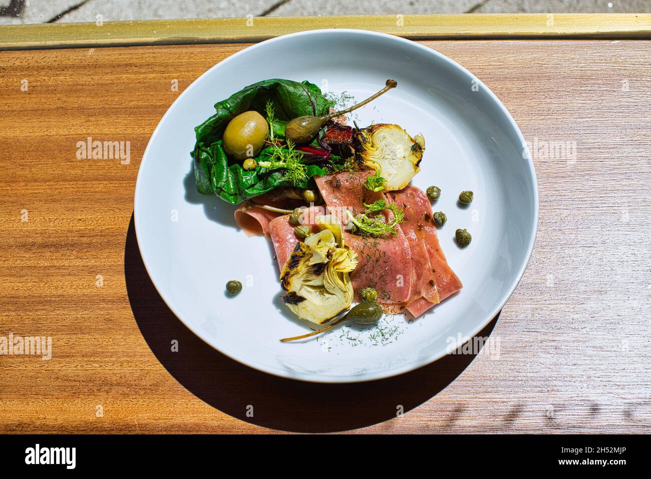 Piatto con insalata con prosciutto, carciofo, olive e capperi su tavola di legno Foto Stock