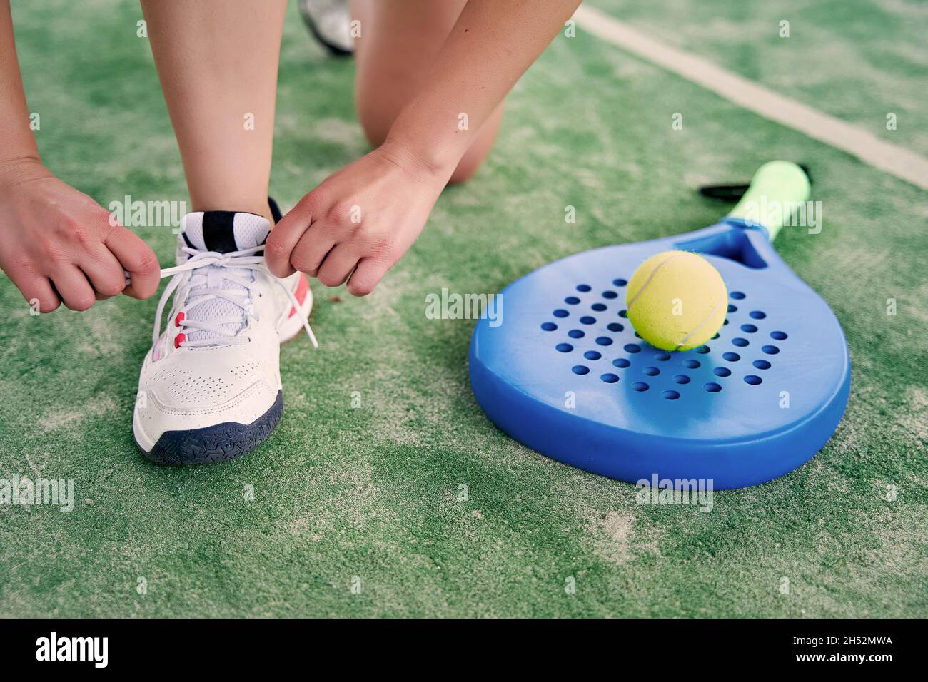 Atleta che lega il pizzo sul campo del padel, con una racchetta e una palla accanto a lei. Foto di alta qualità Foto Stock