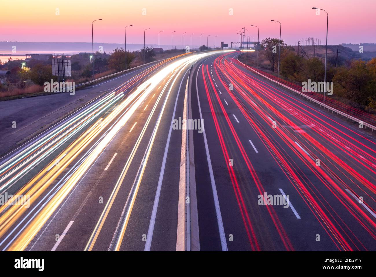 Autostrada suburbana la sera dopo il tramonto. Tracce di traffico intenso dai fari anteriori e dalle luci di posizione posteriori Foto Stock