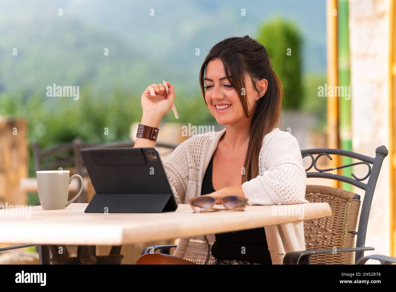 Donna seduta su una terrazza scrivendo su un tablet con penna digitale Foto Stock
