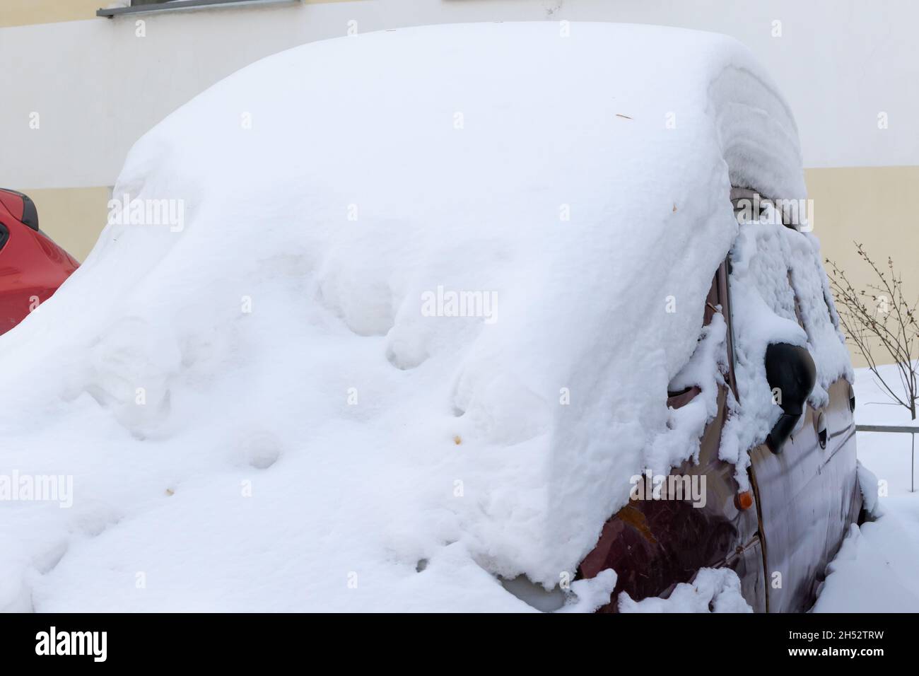 auto abbandonata rossa in inverno parcheggiata sotto un grande strato di neve in un giorno luminoso e soleggiato geloso Foto Stock