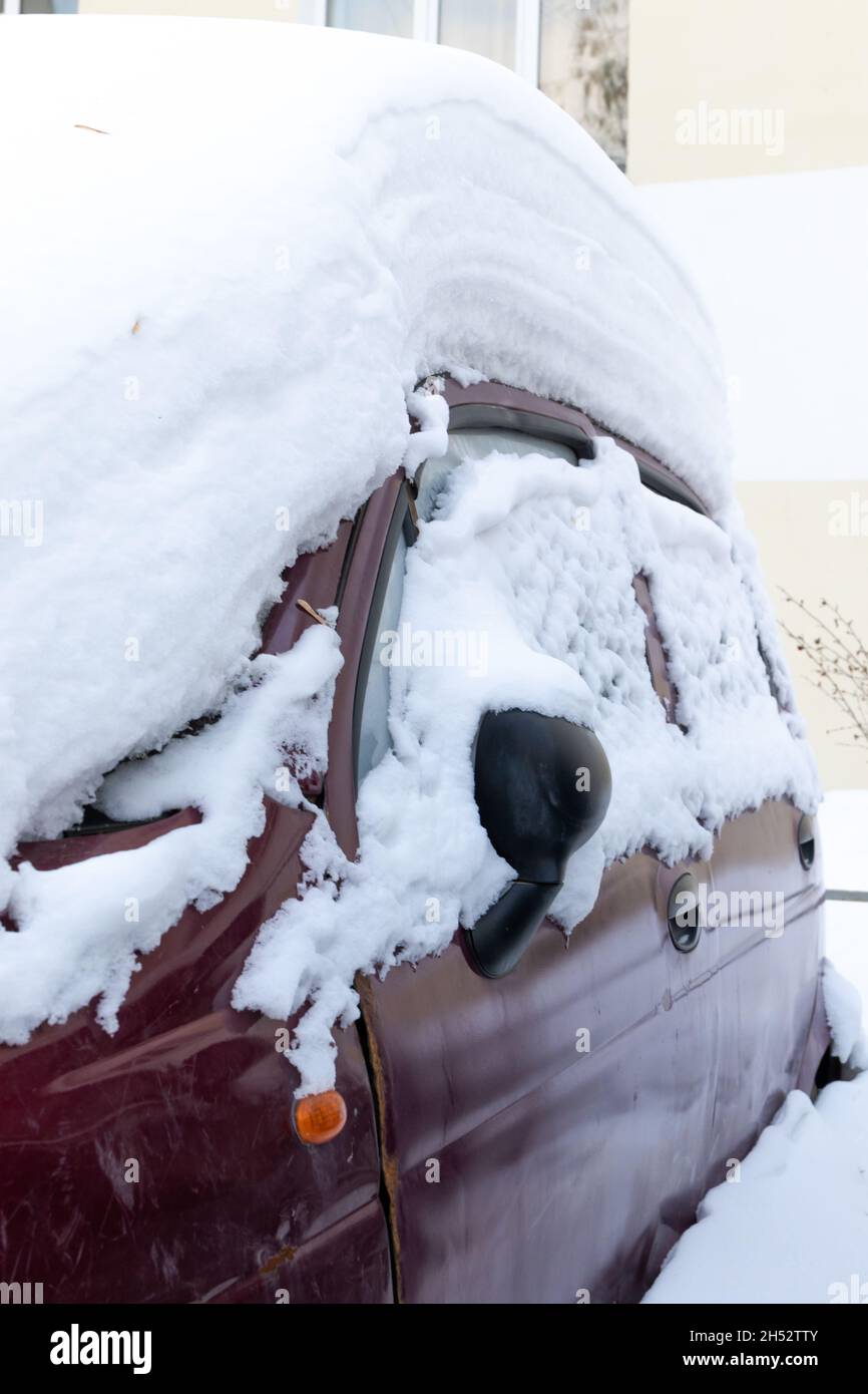 auto abbandonata rossa in inverno parcheggiata sotto un grande strato di neve in un giorno luminoso e soleggiato geloso Foto Stock