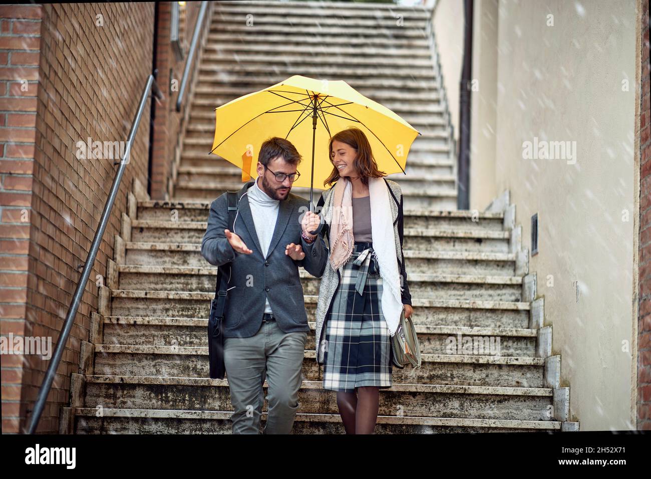 Una giovane coppia innamorata che sta parlando mentre scende le scale in città di buon umore durante una giornata piovosa. Passeggiata, pioggia, città, rapporto Foto Stock