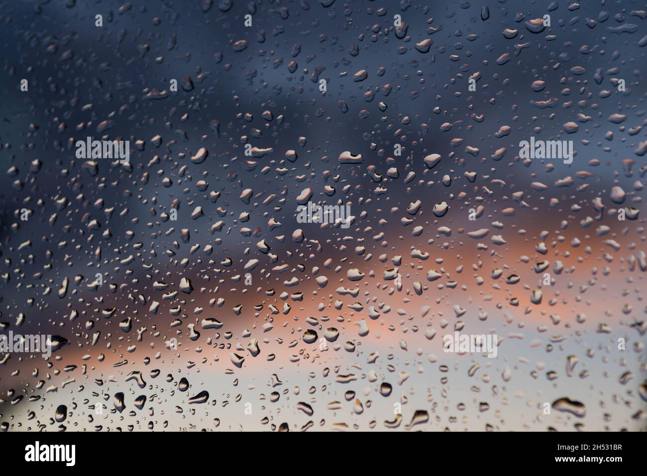 Dopo la pioggia. Il vetro della finestra è coperto all'esterno con gocce d'acqua. Sullo sfondo ci sono nuvole scure. Foto Stock