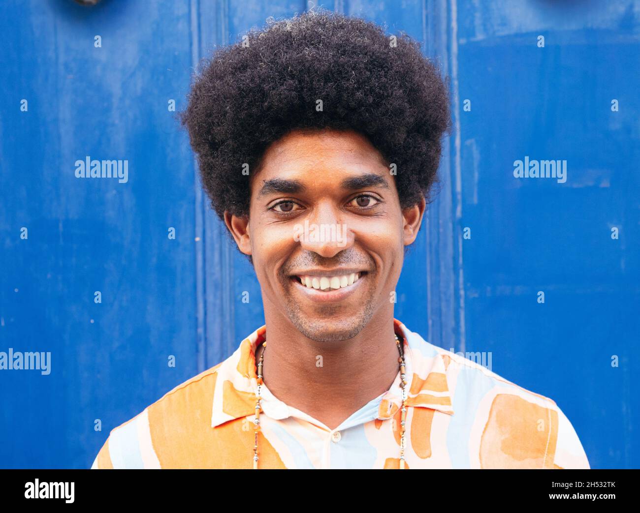 Uomo nero con capelli ricci che sorridono alla fotocamera su uno sfondo blu  della parete Foto stock - Alamy
