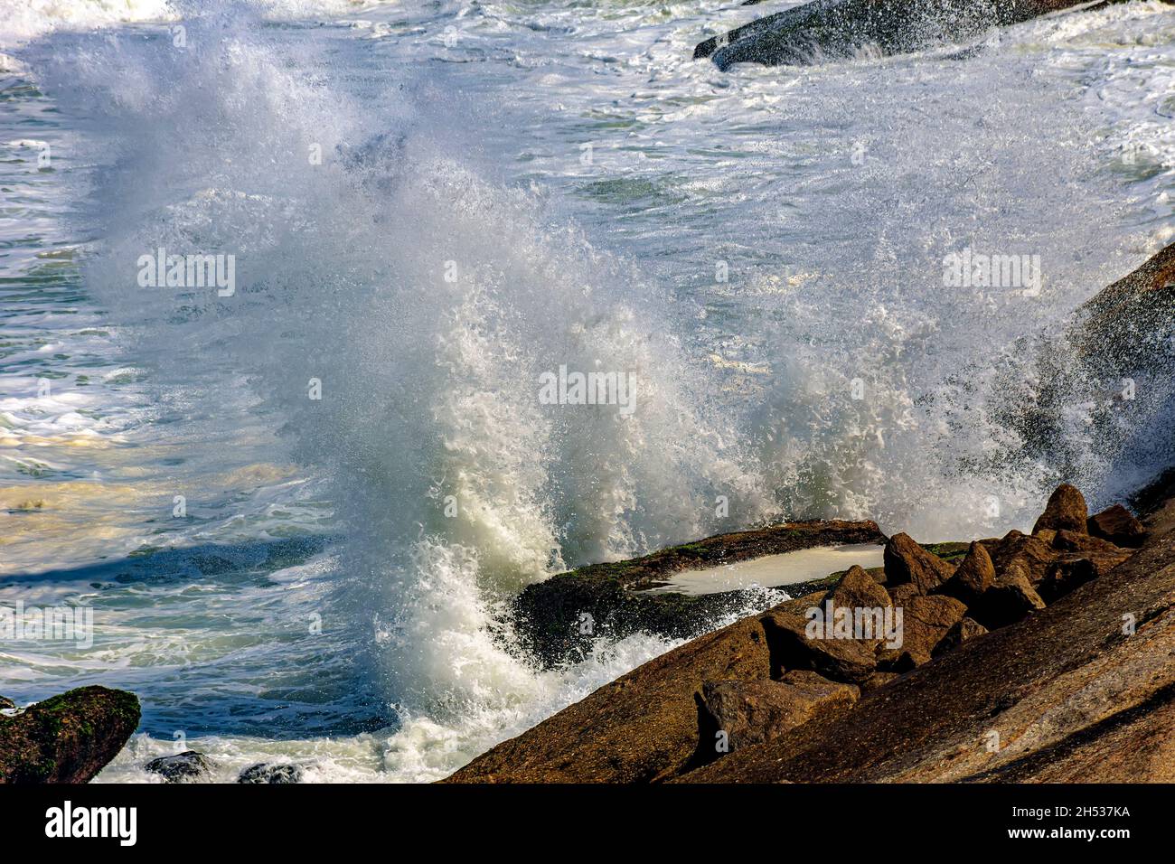 L'acqua di mare si tuffa nell'aria mentre le onde si infrangono contro le rocce Foto Stock