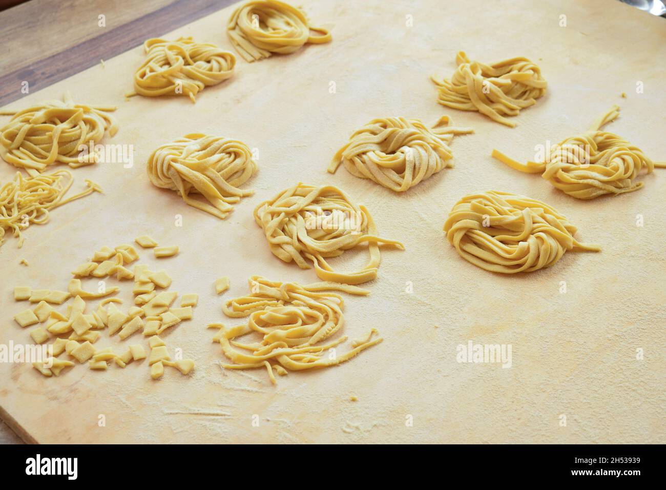 pasta di uova di varietà fatta a mano a casa su un pannello di pasticceria in legno Foto Stock