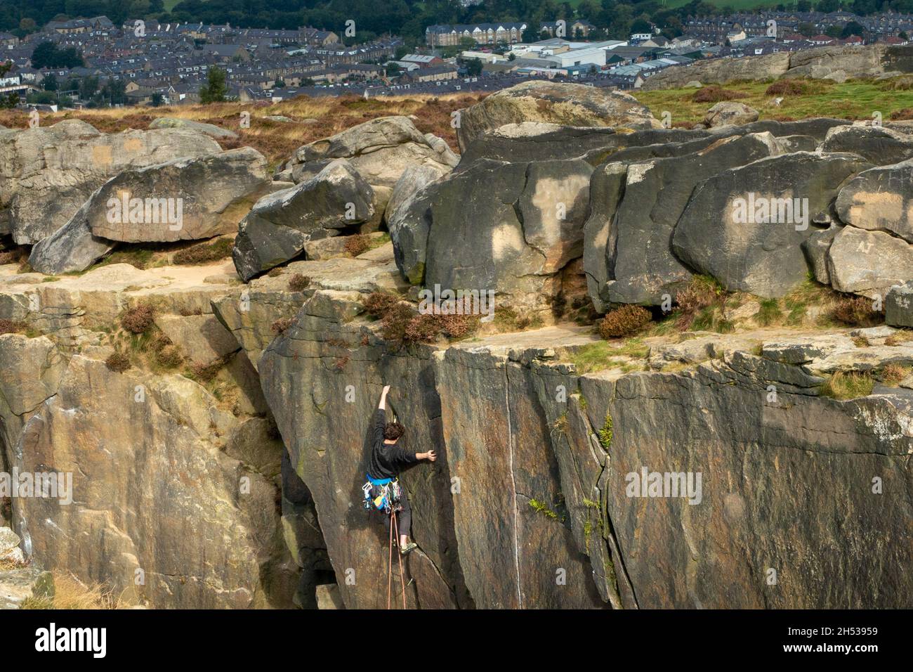 Arrampicatore di roccia che usa l'attrezzatura tradizionale alla cima di una scalata di roccia nella cava di Ilkley al Cow e calf Rocks con vista sulla città di Ilkley. Yorkshire, Regno Unito Foto Stock