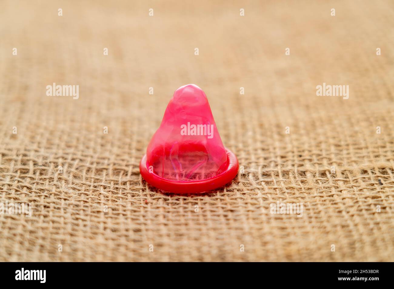 Preservativo rosso posto su una superficie hessiana Foto Stock