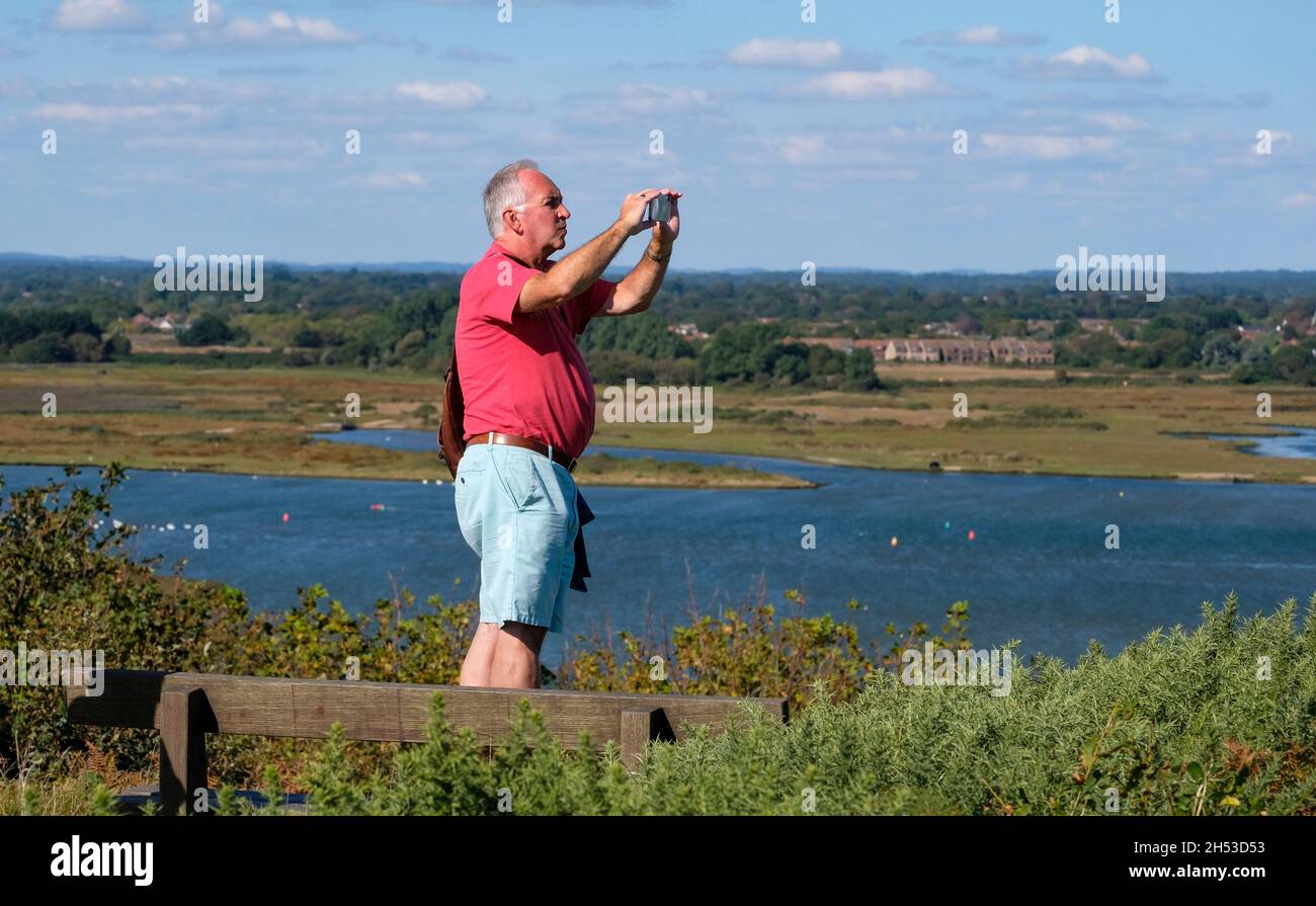 Uomo in piedi scattando una foto di una vista da Hengistbury Head in una giornata di sole nel Dorset Foto Stock