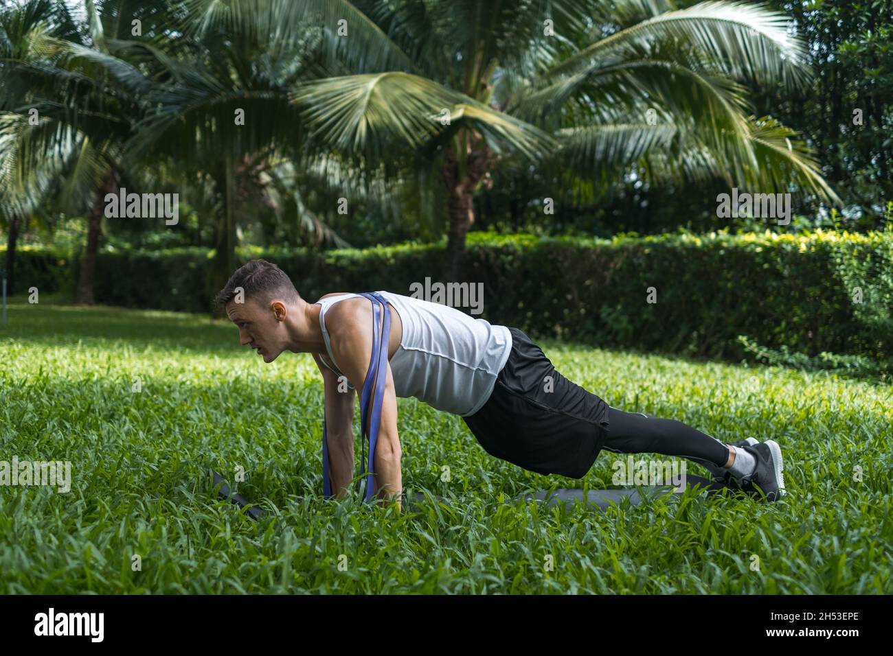 Giovane sportivo e attivo in abbigliamento sportivo che fa esercizi sportivi nel parco. Muscular FIT uomo che fa esercizi con elastico sportivo fascia all'aperto. Foto Stock