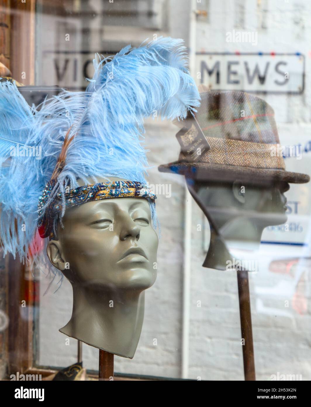 Blue Feather Headress e Tweed Trilby su Mannequin Heads nella finestra di Un negozio Milliner, Lymington UK Foto Stock