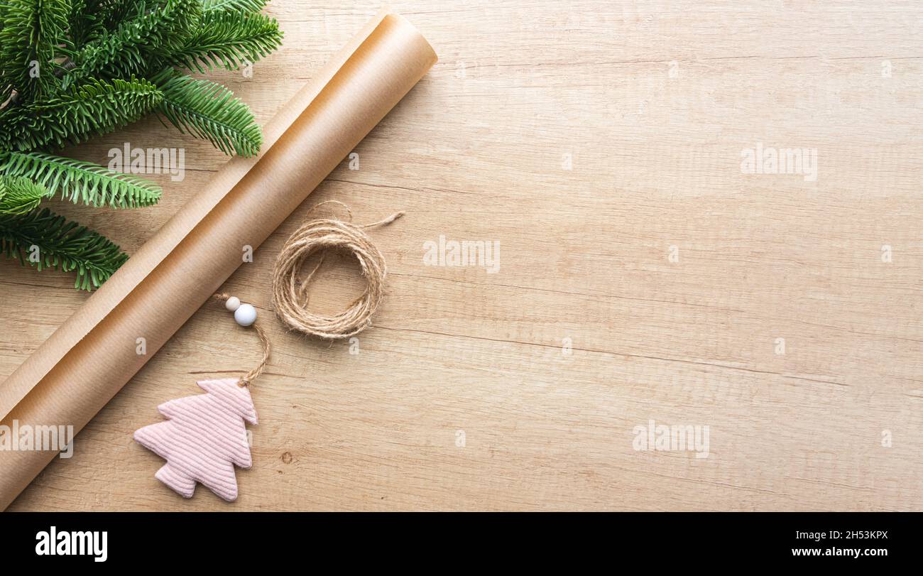 Giocattolo rosa di Natale in forma di albero, un rotolo di carta artigianale e un ramo di abete su uno sfondo di legno con spazio copia, piatto. Imballaggio ecologico Foto Stock