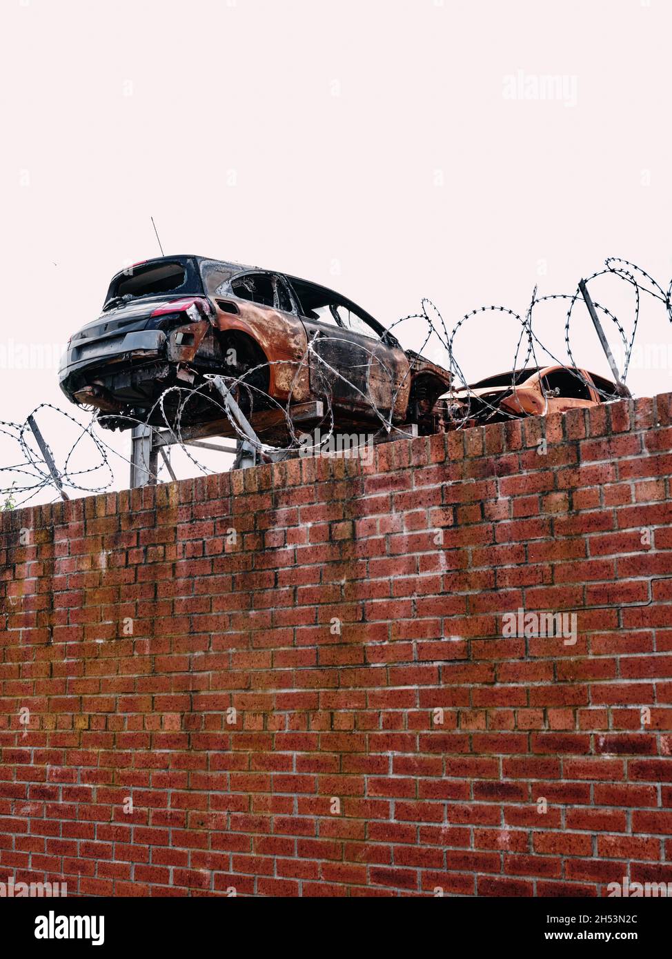 Un rottami di metallo con corpi di auto danneggiati dietro un muro con filo spinato - cantiere di demolitori di auto di metallo - riciclaggio di auto Foto Stock