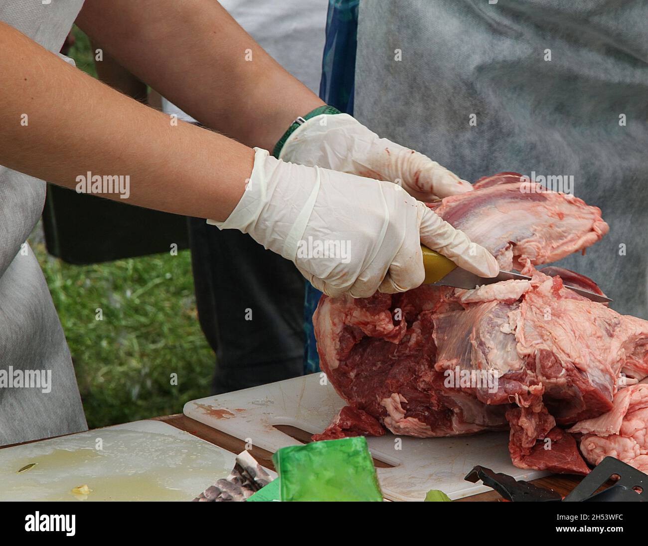 le mani degli uomini in guanti tagliano la carne fresca per strada. cuoci il kebab. Foto Stock