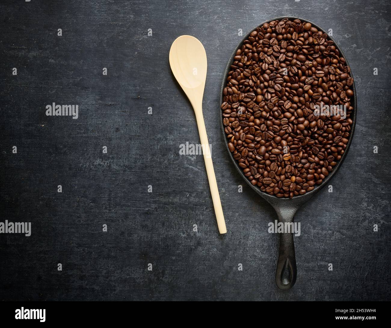 Concetto di tostatura del caffè, cucchiaio di agitazione in legno e padella con chicchi di caffè torrefatti, primo piano, vista dall'alto Foto Stock