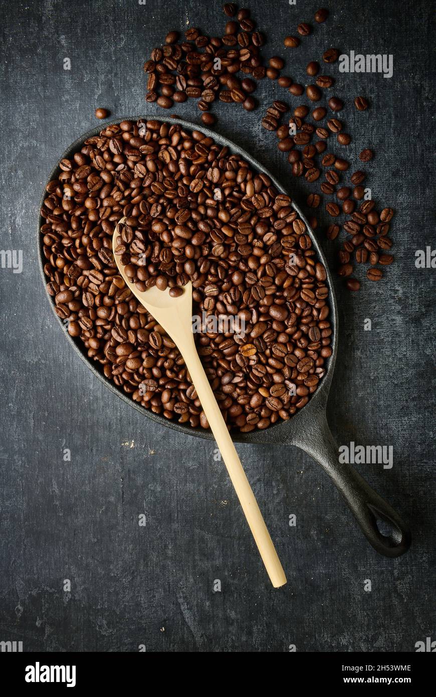 Padella con chicchi di caffè torrefatto e cucchiaino in legno, vista dall'alto Foto Stock
