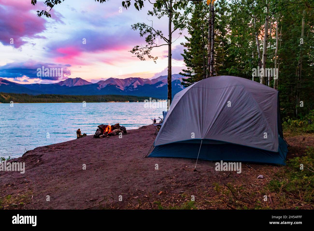 Campeggio perfetto sul lago di Abraham, con sabbia e alberi. Tenda con fuoco illuminato e montagne con tramonto sullo sfondo Foto Stock