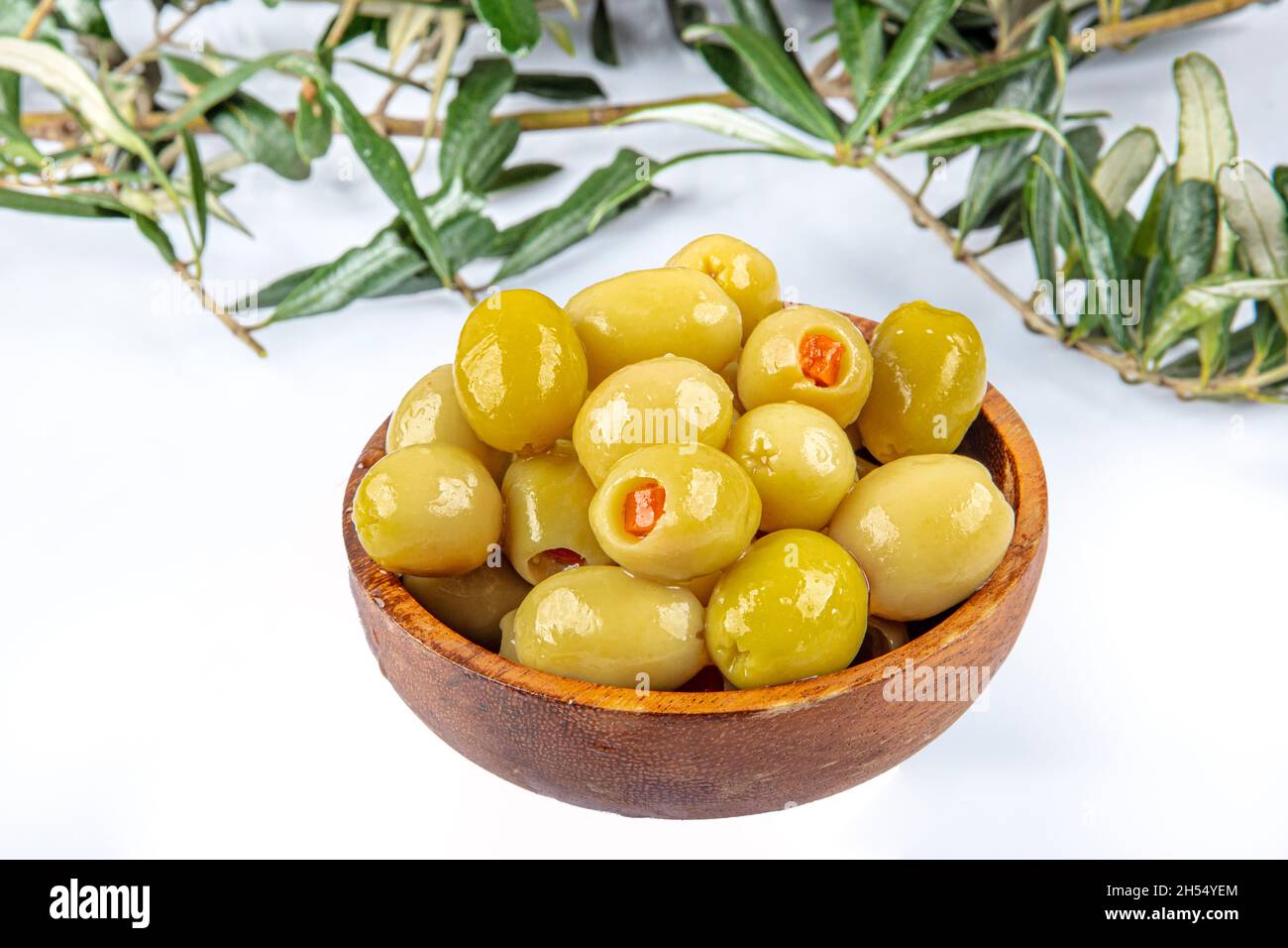 Piccole olive verdi in salamoia, farcite con peperoncino rosso in una ciotola di legno. Frutta di Olea europaea, farcita con fette di peperone. Primo piano da abov Foto Stock