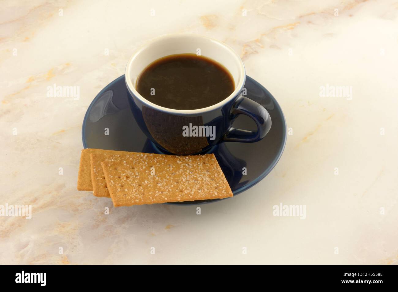 Caffè biscotti e caffè in tazza bianca e blu con piattino sul tavolo Foto Stock