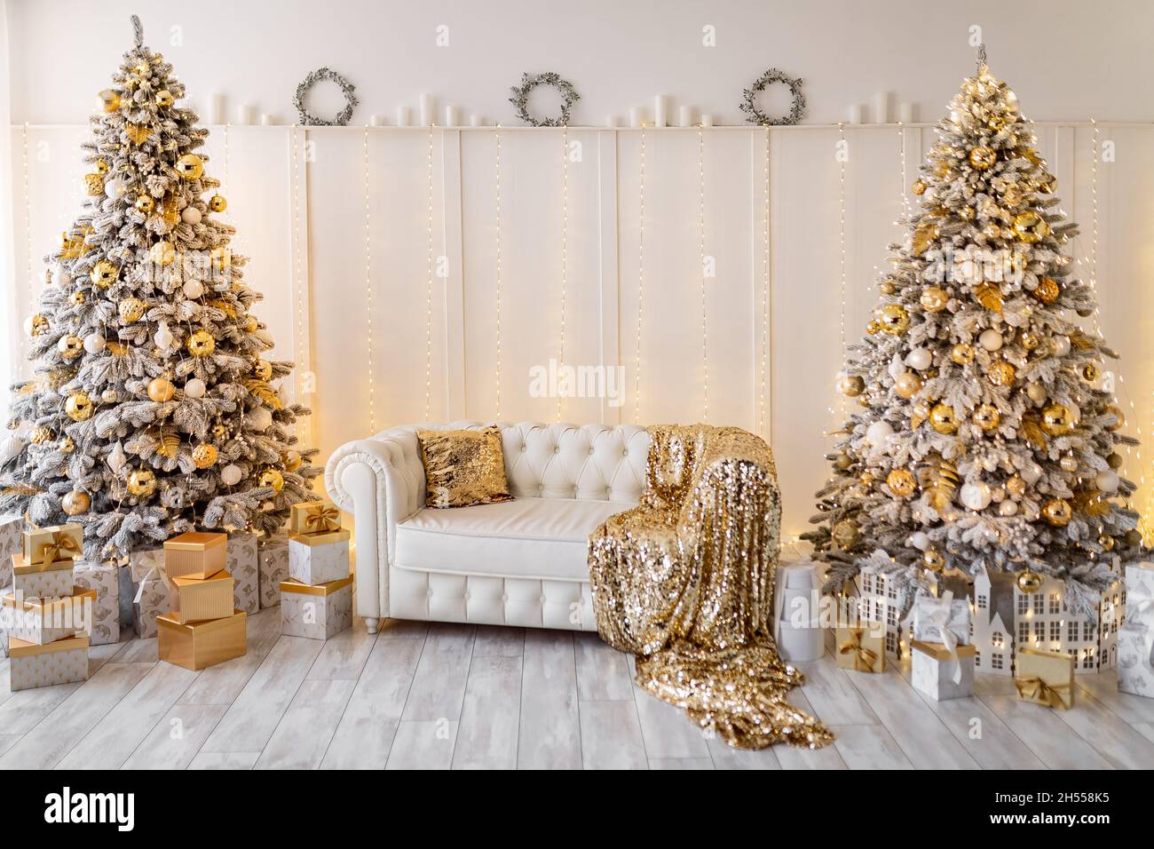Interni bianchi e moderni di natale con due alberi di Natale decorati,  tessuti dorati, regali dorati Foto stock - Alamy