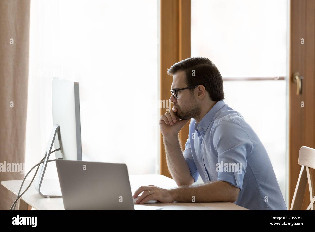 Uomo d'affari giovane e pensivo in occhiali che lavorano al computer. Foto Stock