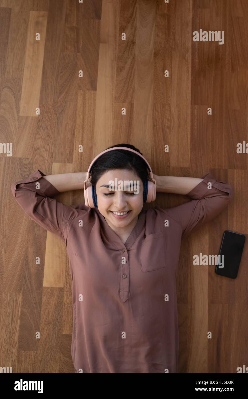 Una donna indiana serena che si trova sul pavimento ascolta la musica con le cuffie Foto Stock