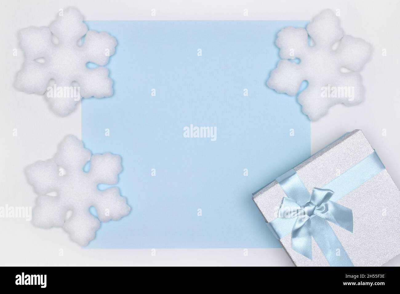 Confezione regalo con decorazioni in fiocco di neve bianco. Spazio di copia. Vacanze invernali sfondo blu Foto Stock