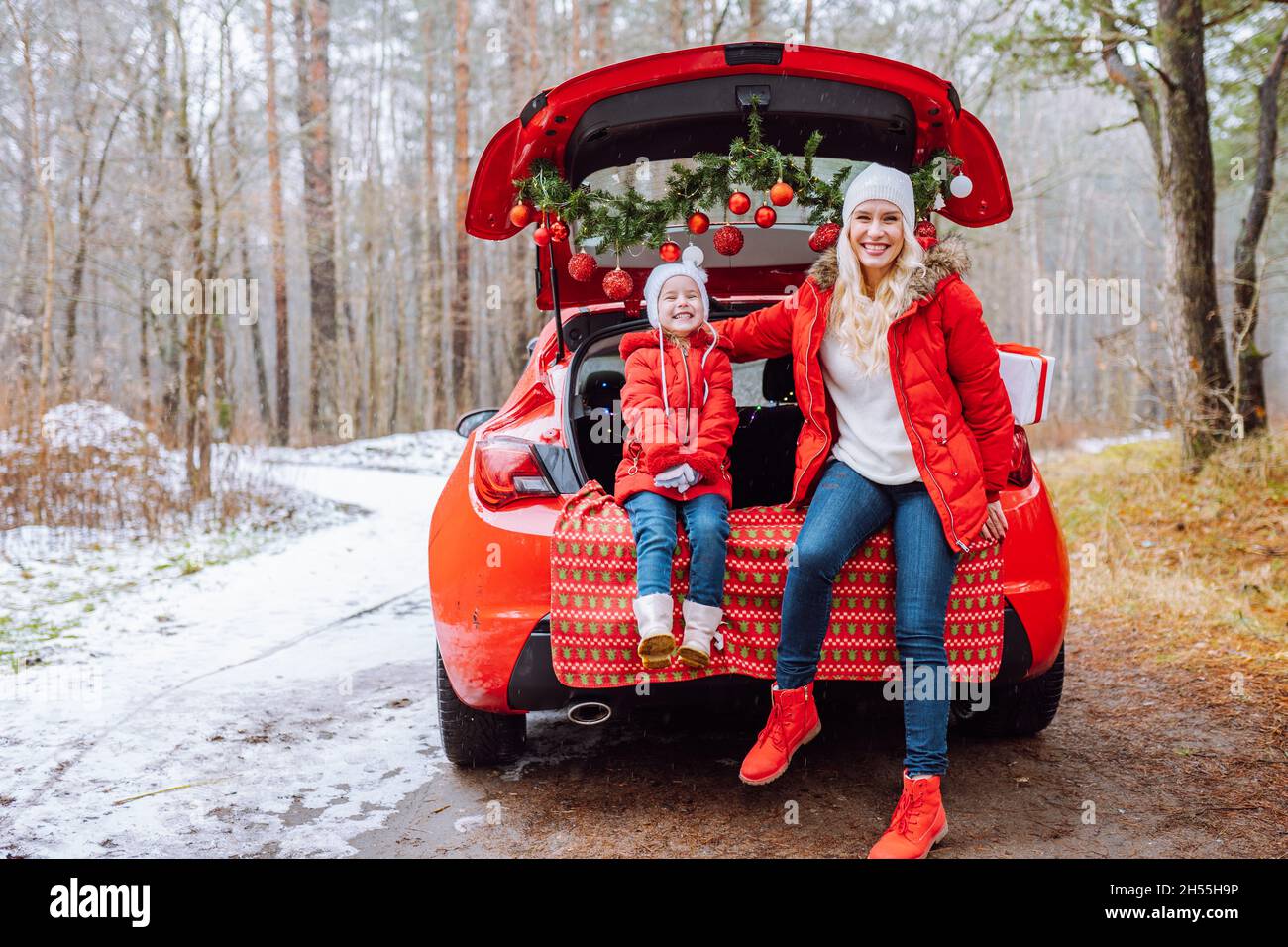 Felice famiglia di mamma bionda e bambina abbracciare l'un l'altro seduto in auto decorata natale nella foresta invernale. Convivenza, vacanze, famiglia Foto Stock