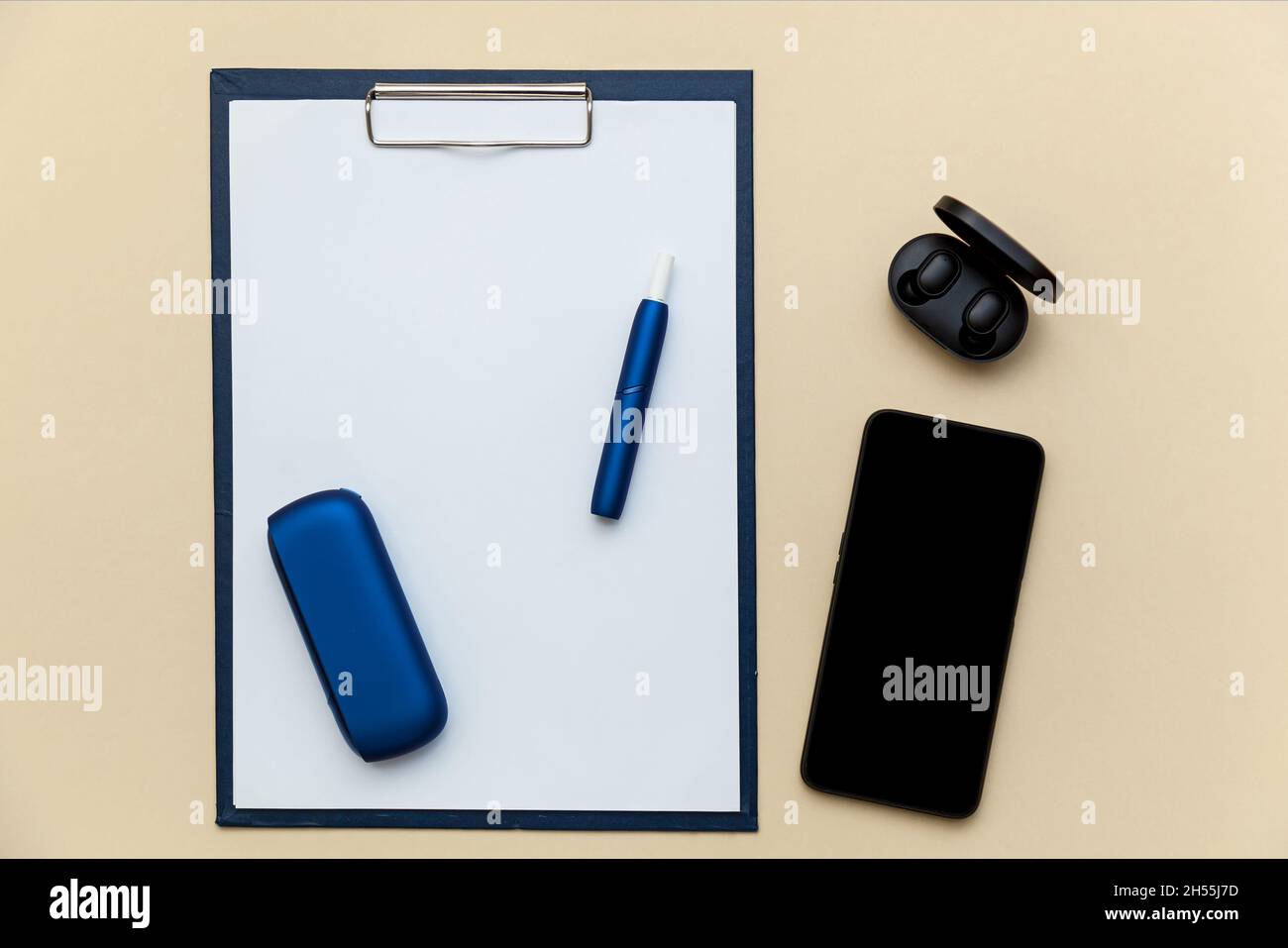 Sigaretta elettronica blu iqos, telefono, cuffie e cartella con clip di carta A4 su sfondo beige. Foto con posto per il testo, il logo e i desi Foto Stock