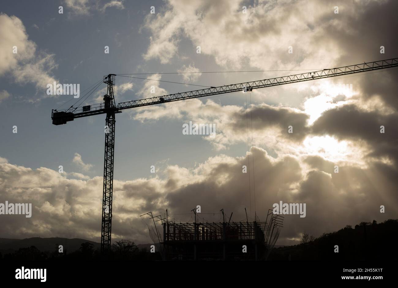 Una gru retroilluminata al tramonto con i raggi del sole che filtrano attraverso le nuvole. Concetto di lavoro e progresso economico Foto Stock